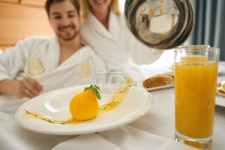 Téléchargez les photos : Joyeuses jeunes mariés dégustent un petit déjeuner au champagne, la table est posée sur un grand lit - en image libre de droit