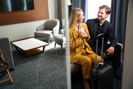 Téléchargez les photos : Couple heureux enregistré dans une chambre d'hôtel, les gens en combinaison de voyage et avec une valise - en image libre de droit