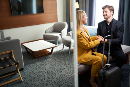 Photo for Man and a woman checked into a hotel room, people in traveling suits and with a suitcase - Royalty Free Image