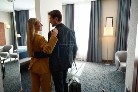 Téléchargez les photos : Guy et sa copine se serrent dans leurs bras dans une chambre d'hôtel, l'homme a une valise de voyage - en image libre de droit