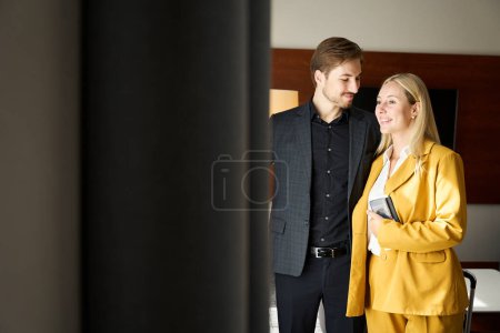Photo for Traveling couple standing at window in hotel room, woman in yellow travel suit - Royalty Free Image
