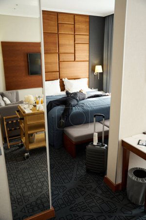 Téléchargez les photos : Voyageur couché les bras tendus sur un grand lit dans une chambre d'hôtel, il est en noir vêtements de voyage - en image libre de droit