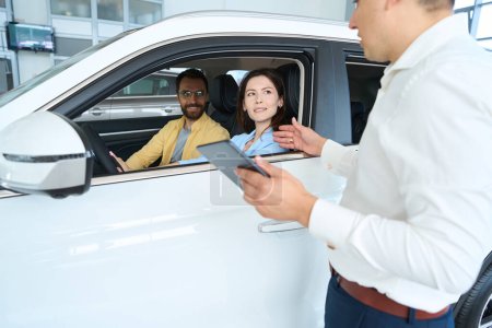 Manager advises a couple before a test drive of a new car, the couple is seated in the cars interior
