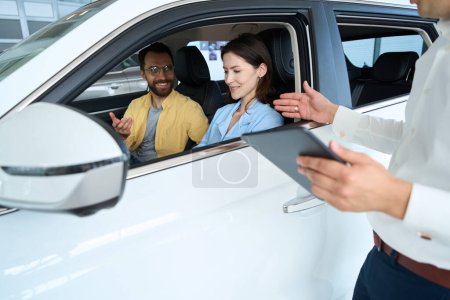 Foto de Gerente aconseja a los cónyuges antes de una prueba de conducción de un coche nuevo, la pareja está sentada en el interior del coche - Imagen libre de derechos