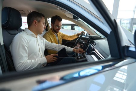 Téléchargez les photos : Acheteur avec un manager dans la voiture, le client étudie la fonctionnalité d'un modèle populaire - en image libre de droit