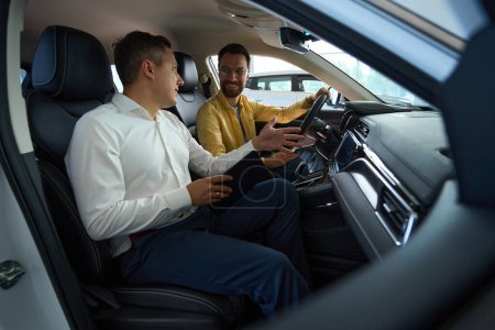 Foto de Cliente con un consultor en el interior de un coche moderno, el comprador estudia la funcionalidad de un modelo popular - Imagen libre de derechos