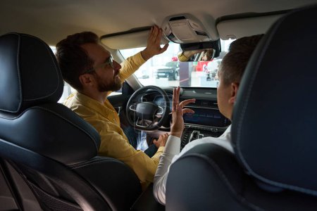 Téléchargez les photos : Gestionnaire et client sont assis à l'intérieur de la voiture moderne, l'acheteur étudie la fonctionnalité d'un modèle populaire - en image libre de droit