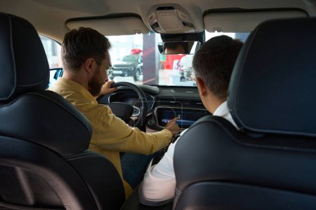 Foto de Los hombres se sientan en el interior de un coche moderno, el comprador estudia la funcionalidad de un modelo popular - Imagen libre de derechos