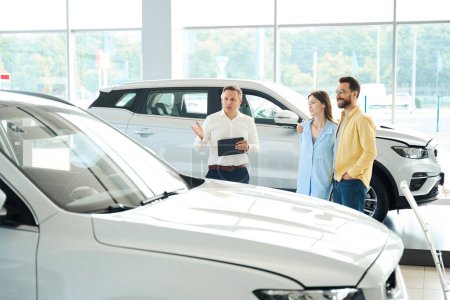 Photo for Customer service manager presents a popular car model to customers, a couple leases a car - Royalty Free Image