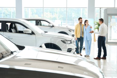 Photo for Customer service manager consults people in a car dealership, people choose a car - Royalty Free Image