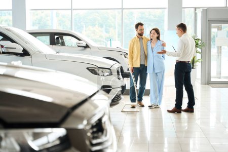 Photo for Customer service manager consults a couple in a car dealership, people choose a car - Royalty Free Image