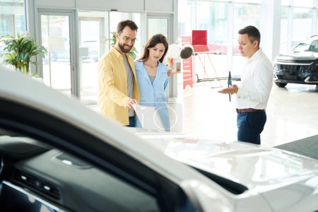 Foto de Pareja en un concesionario de automóviles se comunica con un consultor, la gente elige un modelo de coche popular - Imagen libre de derechos