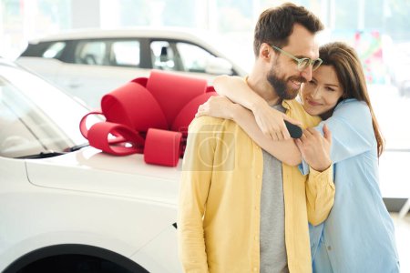 Foto de Mujer feliz abrazando a su amado marido, pareja de pie cerca del coche con arco de regalo - Imagen libre de derechos