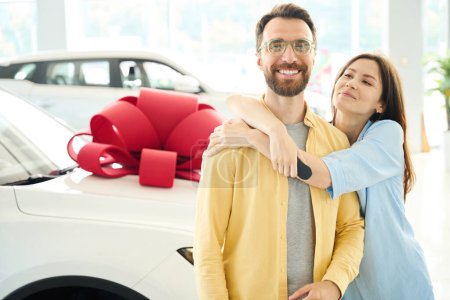 Foto de Mujer alegre abrazando a su amado marido, pareja de pie cerca del coche con arco de regalo - Imagen libre de derechos