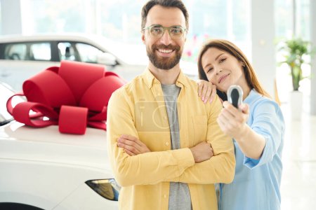 Téléchargez les photos : Couple se tient près d'une voiture avec un arc cadeau, la femme a des clés de voiture dans ses mains - en image libre de droit