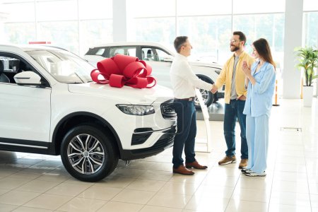 Photo for Buyer and the manager sealed the deal with a handshake, the husband gives the car to his beloved wife - Royalty Free Image
