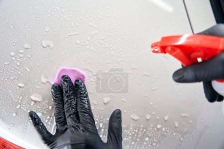 Foto de Proceso simple de aplicar arcilla especial en los detalles del coche, un reparador utiliza una botella de aerosol - Imagen libre de derechos