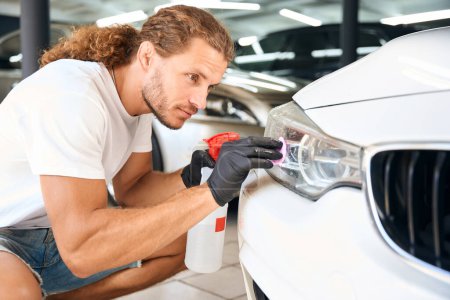 Photo for Unshaven male uses special clay in car detailing, the guy works with headlights - Royalty Free Image