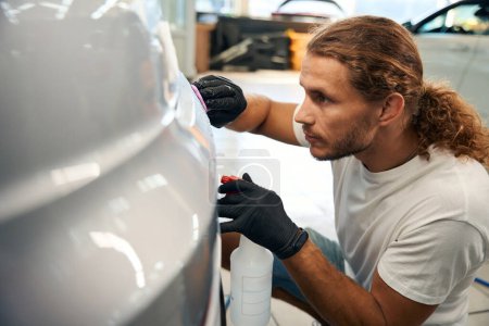 Photo for Young man works with special clay in car detailing, a spray bottle is used in the work - Royalty Free Image