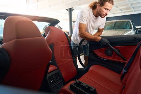 Foto de El hombre con guantes protectores aspira el interior de un coche, utiliza una potente aspiradora - Imagen libre de derechos