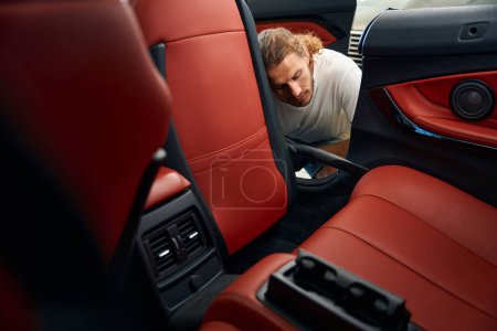 Foto de Hombre sin afeitar aspira el interior de un coche, utiliza una herramienta de grieta - Imagen libre de derechos