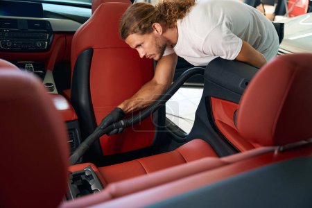 Téléchargez les photos : Le gars aspire l'intérieur d'une voiture, il nettoie les sièges arrière - en image libre de droit