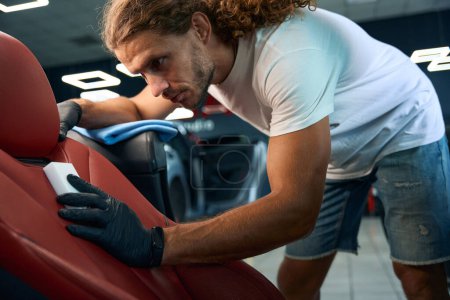 Téléchargez les photos : Homme nettoie un siège conducteur en cuir avec une éponge de mélamine, il fait des détails pour l'intérieur d'une voiture élégante - en image libre de droit