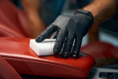 Master in protective gloves cleans a leather armrest, he uses a melamine sponge