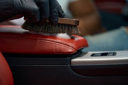 Foto de El hombre limpia un reposabrazos de cuero con un cepillo y espuma, que está haciendo los detalles interiores del coche - Imagen libre de derechos