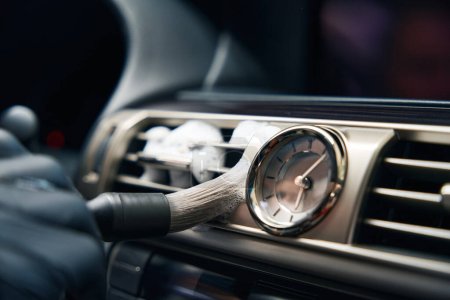 Foto de El hombre limpia un conducto de aire del coche con un cepillo especial, hay un reloj en el salpicadero - Imagen libre de derechos