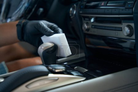 Téléchargez les photos : Homme en gants de protection nettoie une pièce de voiture avec une éponge de mélamine, il est assis dans le siège du conducteur - en image libre de droit
