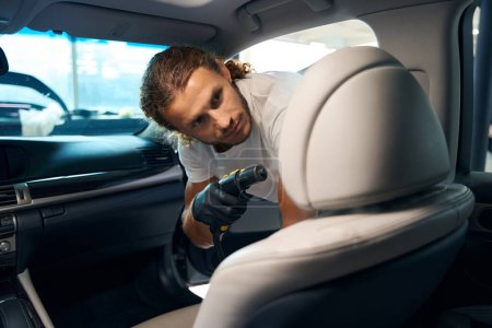 Foto de Hombre sin afeitar limpia el asiento delantero de un coche elegante con un generador de vapor, que hace los detalles interiores - Imagen libre de derechos