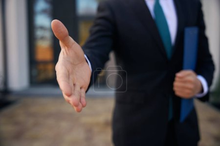 Photo for Close up photo of man hand, who giving it for handshake and holding a folder in another hand - Royalty Free Image