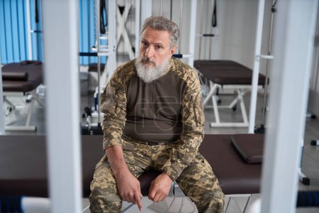 Téléchargez les photos : Homme militaire barbu assis dans la salle de gym d'un centre de réadaptation, un homme en tenue de camouflage - en image libre de droit