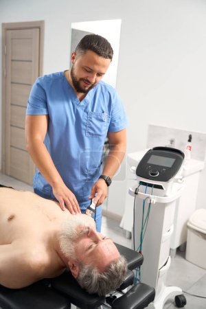 Foto de Médico fisioterapeuta utiliza métodos de tratamiento eficaces para el paciente, el hombre tiene barba gris - Imagen libre de derechos