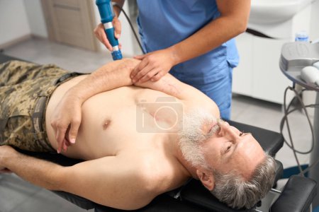 Photo for Doctor working with elbow of gray-haired patient, man lying on couch with naked torso - Royalty Free Image