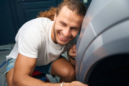 Téléchargez les photos : Homme heureux étreignant sa voiture préférée, voiture subissant des détails dans l'atelier de réparation automobile - en image libre de droit