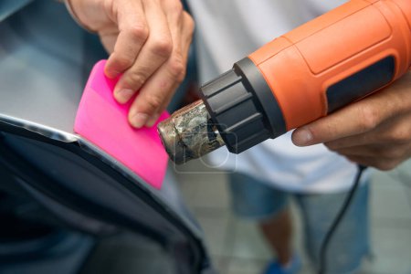 Using an industrial dryer when detailing a car, the master glues anti-gravel film to the car doors