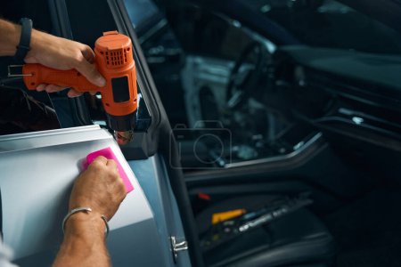 Using a powerful industrial dryer when detailing a car, a repairman glues anti-gravel film on car doors