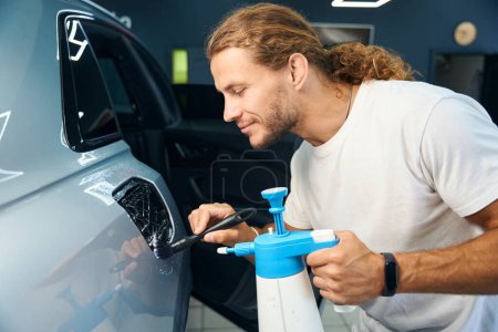 Male works in a car repair shop detailing a white car, he uses special devices