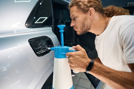 Foto de Master utiliza una botella de spray en el proceso de detalle del coche, limpia la superficie del cuerpo - Imagen libre de derechos