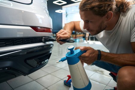 Foto de Macho utiliza un cepillo suave y una botella de spray en el proceso de detalle del coche para limpiar las rejillas - Imagen libre de derechos