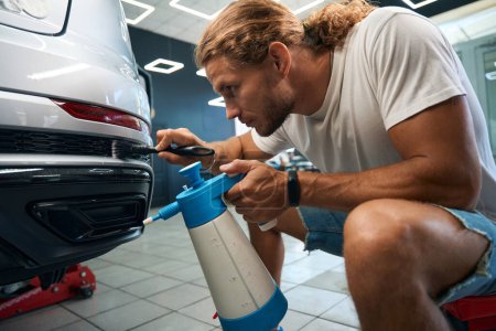 Male cleans car body grilles with a soft brush, car detailing process in auto repair shop