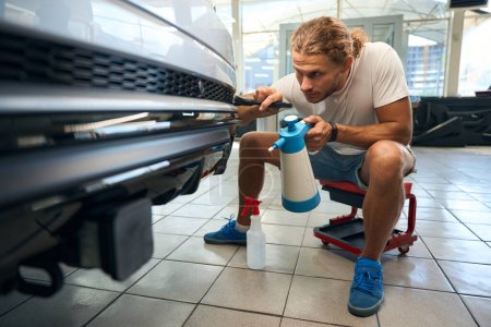 Young guy cleans the car body grilles with soft brush, the process of car detailing in an auto repair shop
