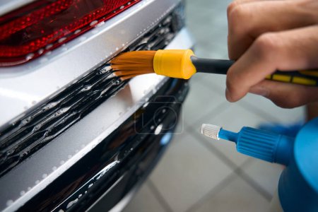 Téléchargez les photos : Guy nettoie les grilles de voiture avec une brosse spéciale et utilise également un vaporisateur - en image libre de droit