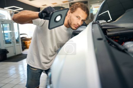Photo for Male conducts a control inspection of the car body, he uses a powerful lamp - Royalty Free Image