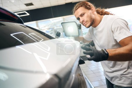 Téléchargez les photos : Mécanicien automobile effectue une inspection de contrôle de la carrosserie de la voiture, il utilise une lampe puissante - en image libre de droit