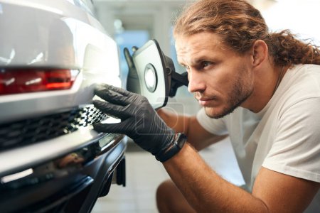 Foto de Chico en un taller de reparación de automóviles está llevando a cabo una inspección de la carrocería del coche, él tiene una poderosa lámpara - Imagen libre de derechos