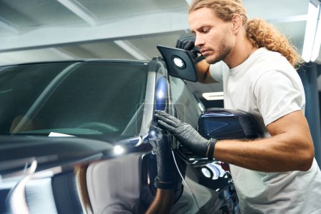 Photo for Man conducts a check inspection of a car using a powerful lamp - Royalty Free Image