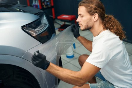 Photo for Man is gluing anti-gravel film onto the body of a car, he works wearing protective gloves - Royalty Free Image